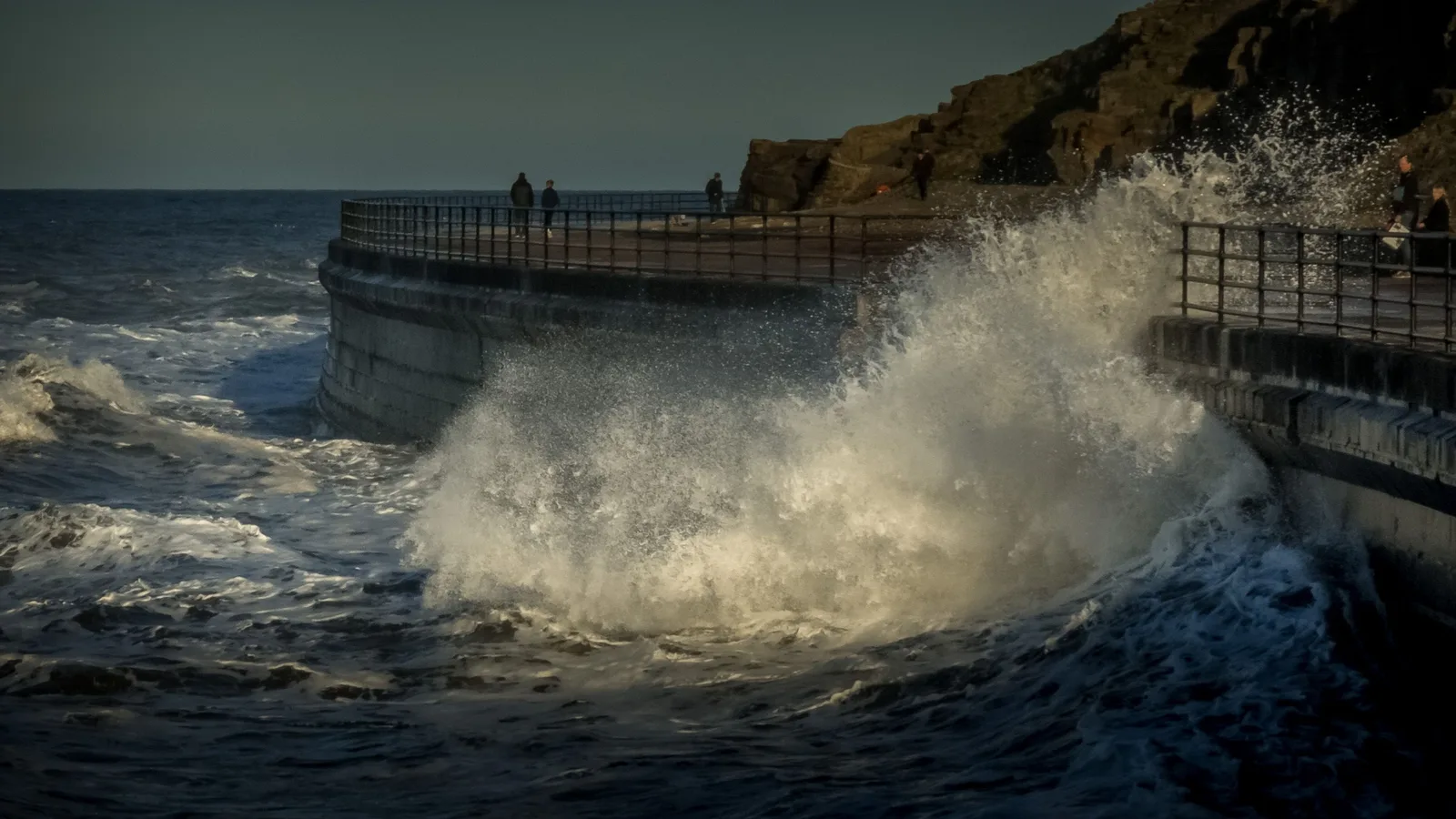 Powerful ocean waves crashing against a seawall with a dramatic background.