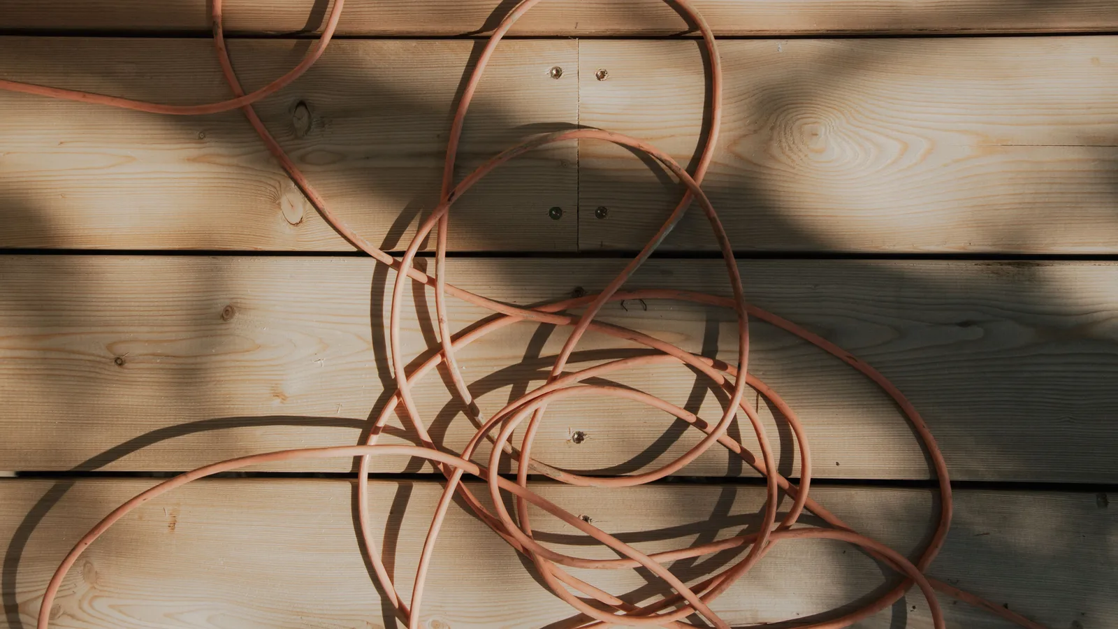 Tangled orange extension cord lying across sunlit wooden deck boards
