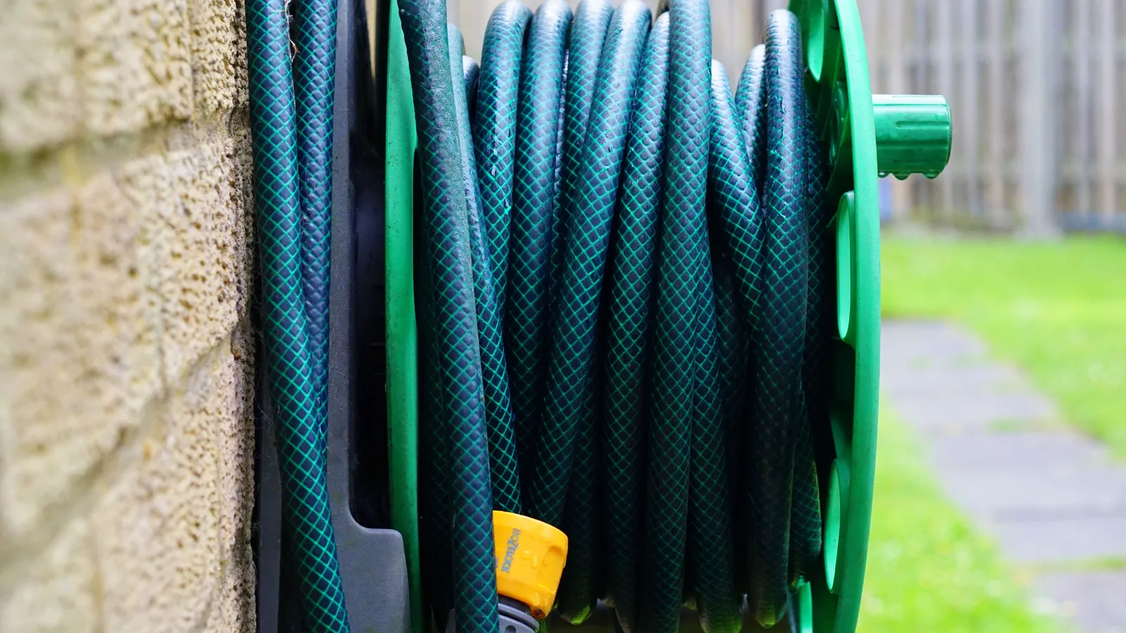 Dark garden hose coiled on a green reel mounted outside a stone wall