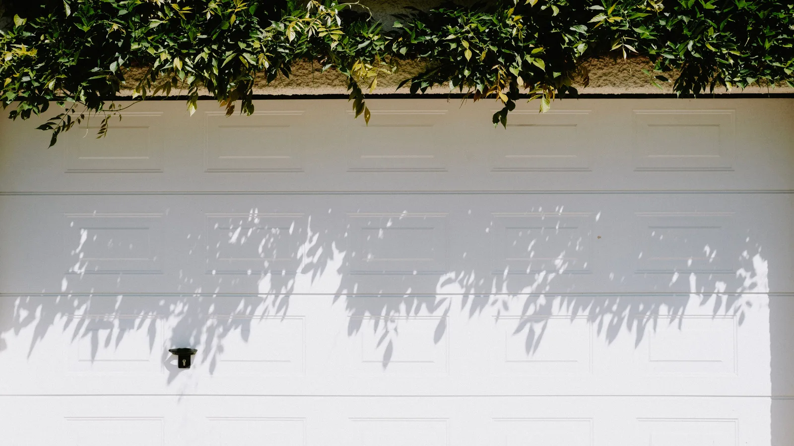 Closed white sectional garage door with the rigid lower section visible below the horizontal joint