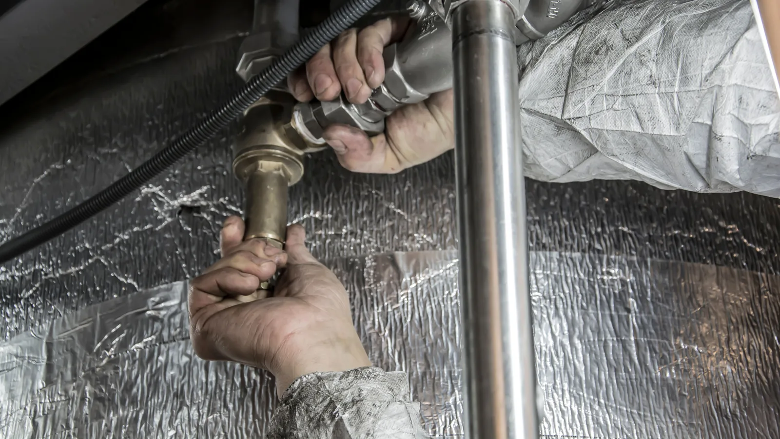 Close-up of a plumber's hands installing steel pipes indoors, showcasing skilled manual work.