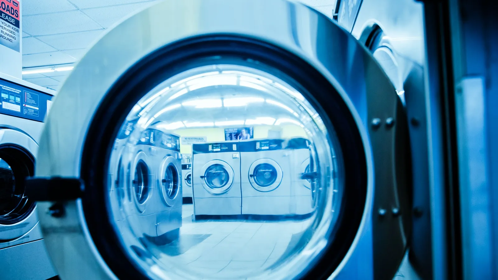 Interior view of a modern laundromat with rows of steel washing machines.